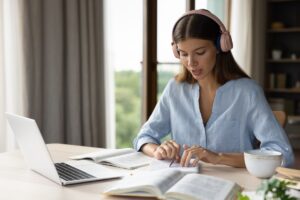 une femme avec des livres et son ordinateur se prépare à passer la certification cloe ou toeic